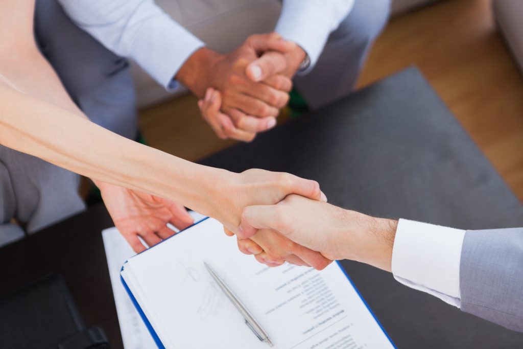 Salesman shaking hand with client with contract on the coffee table